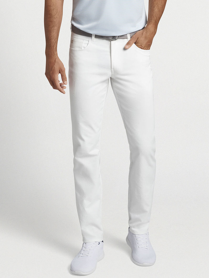 A person wearing a light blue shirt and Peter Millar Performance Five-Pocket Pant in White, featuring moisture-management technology, stands against a plain background.