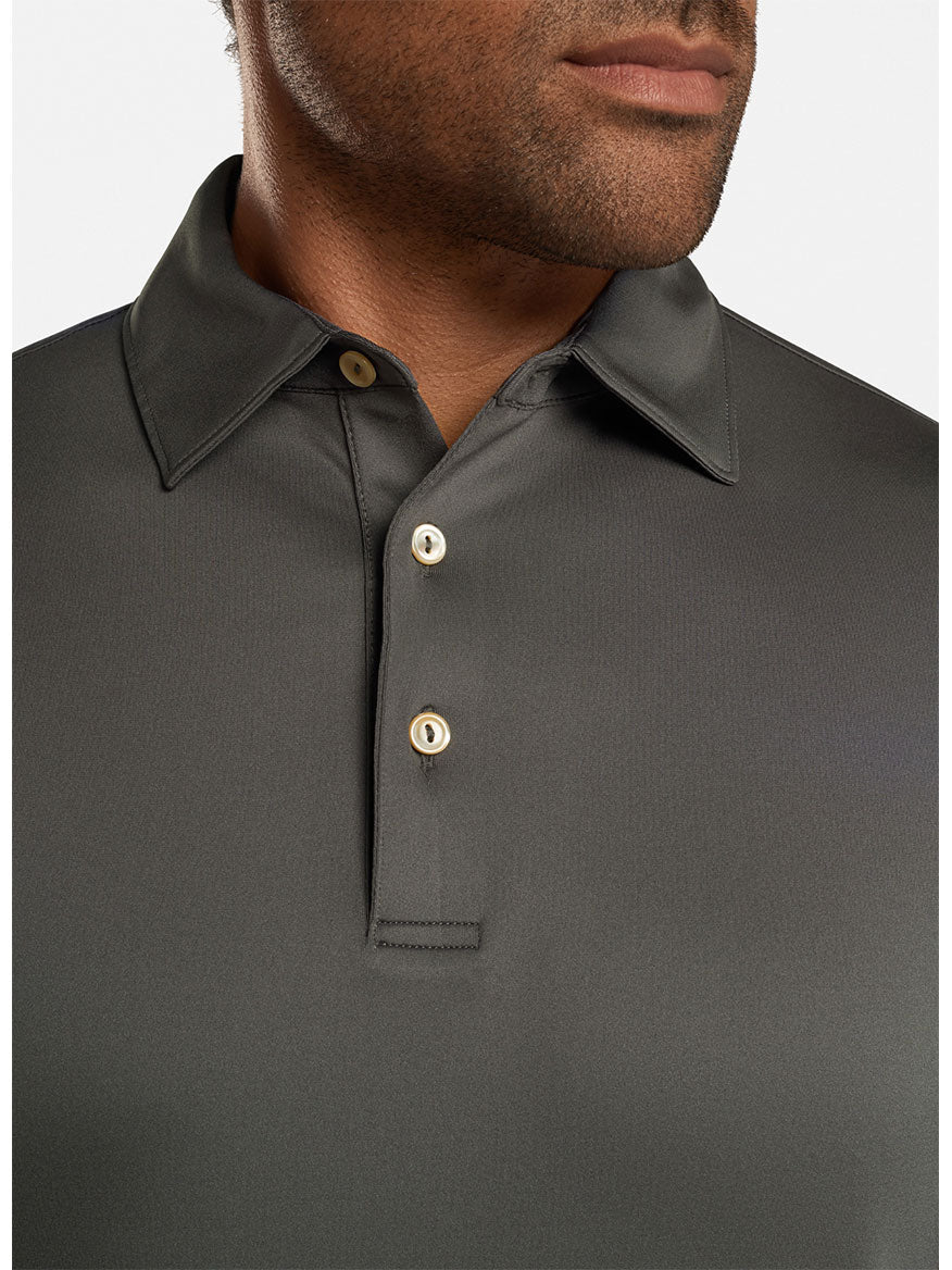 A man wearing the Peter Millar Solid Performance Jersey Polo in Iron featuring a Sean self-collar and three buttons visible.