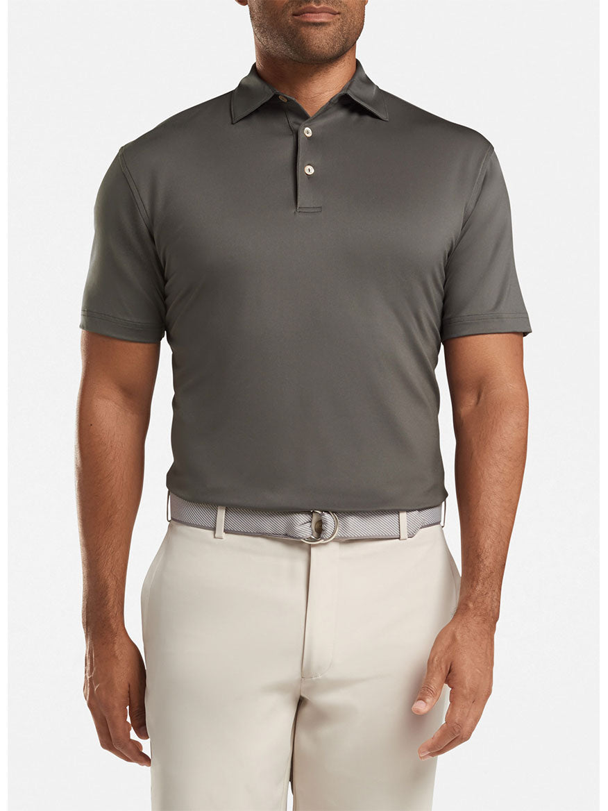 A man wearing a Peter Millar Solid Performance Jersey Polo in Iron with a Sean self collar and light-colored pants stands against a plain background.