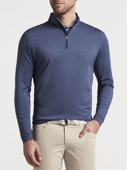A man wearing a blue Peter Millar Perth Melange Performance Quarter-Zip in Navy and beige pants, standing against a neutral background.