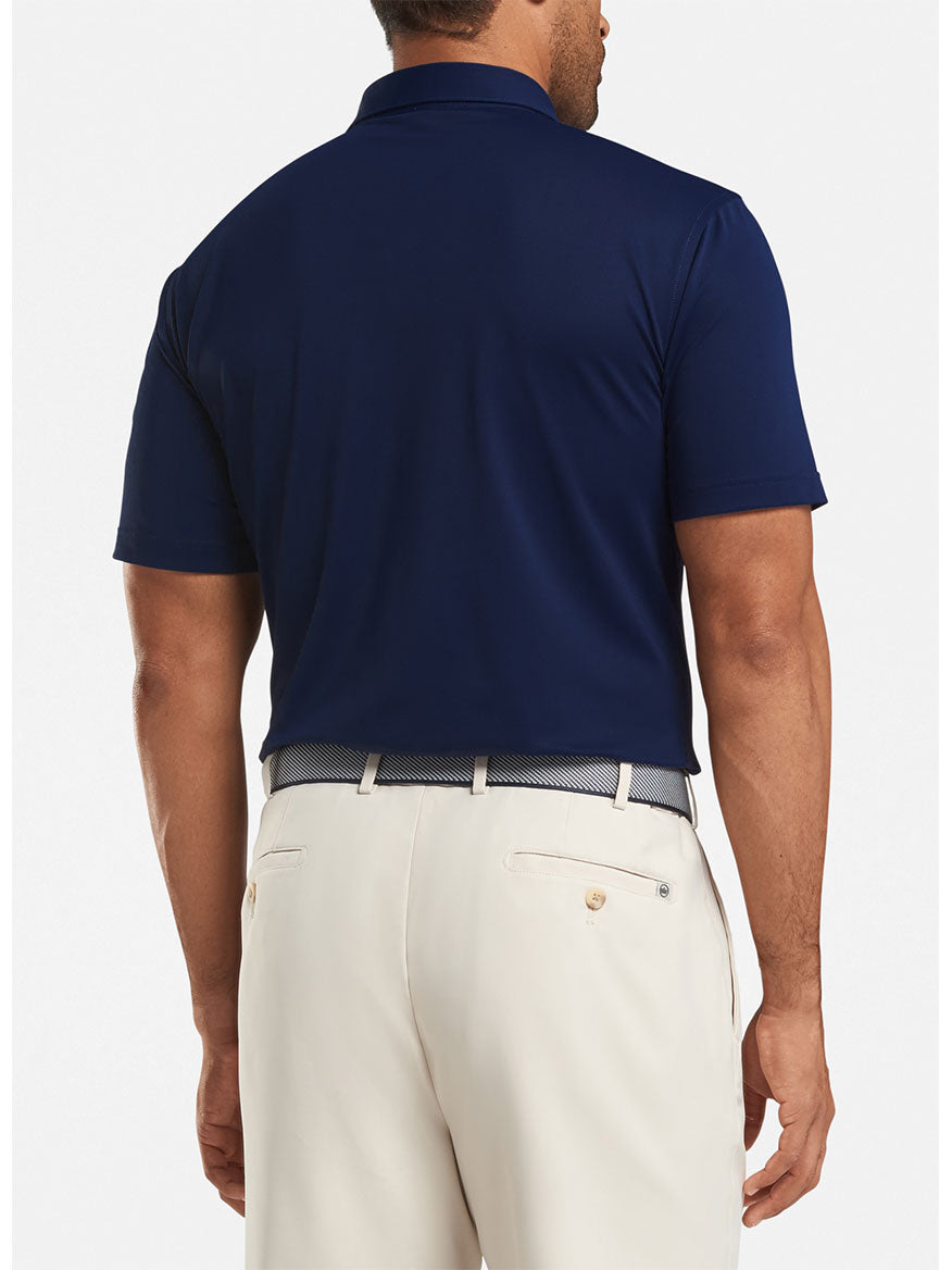 A man is seen from behind wearing the Peter Millar Solid Performance Mesh Polo in Navy, tucked into light beige trousers and paired with a patterned belt.