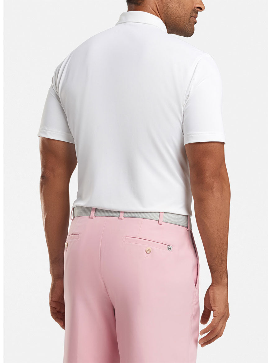 Man standing with his back to the camera, wearing a Peter Millar Solid Performance Mesh Polo in White, light pink trousers, and a light gray belt.