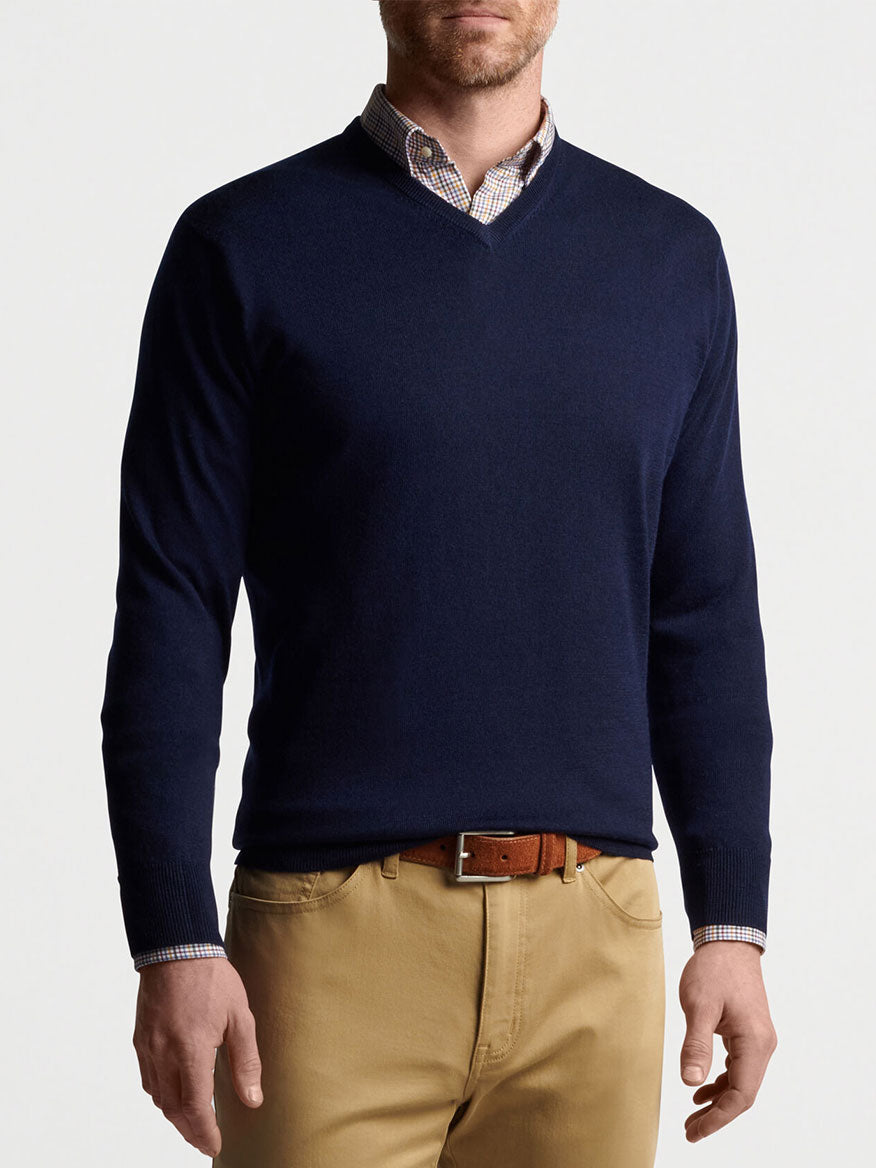 A man wearing a Peter Millar Autumn Crest V-Neck in Navy made of Merino wool in a soft blue shade, paired with comfy khaki pants.