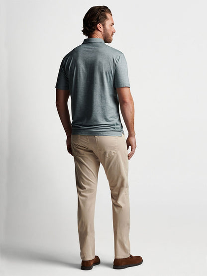 Man standing in profile view wearing a grey polo shirt and tailored fit, garment dyed Peter Millar Wayfare Five-Pocket Pant in Stone.