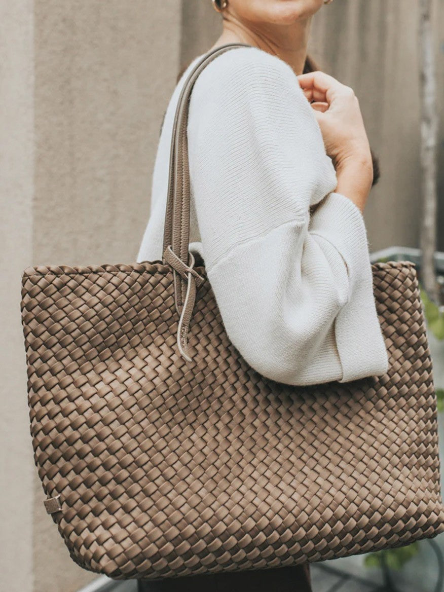 A woman in a white sweater carrying a large Naghedi Jetsetter Small Tote in Solid Onyx over her shoulder.