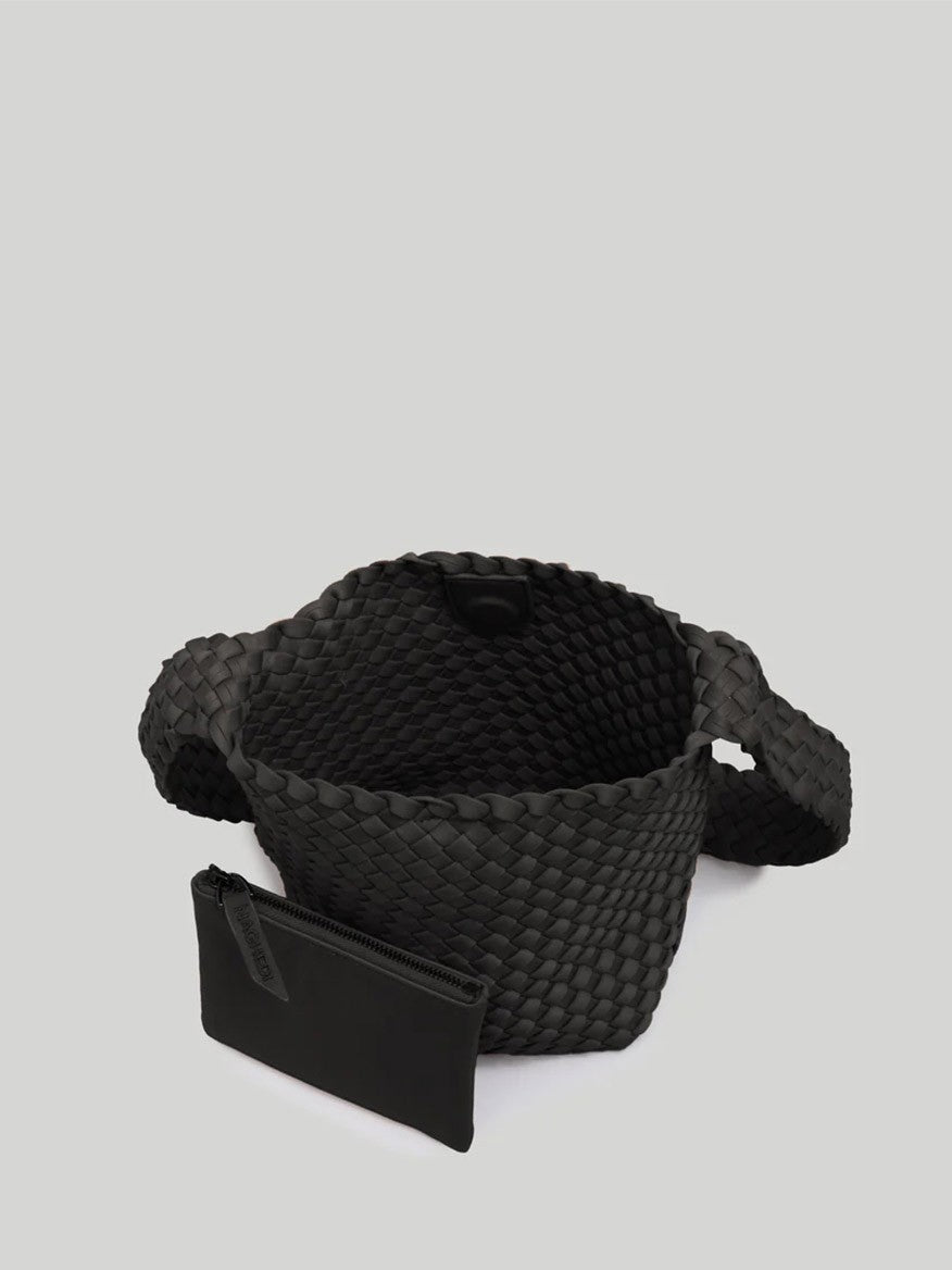 A Naghedi Laguna Crossbody in Solid Onyx with short handles and an open top, accompanied by a small black zippered pouch placed in front of it against a plain gray background. This stylish everyday bag features a wide weave strap, adding both functionality and flair.