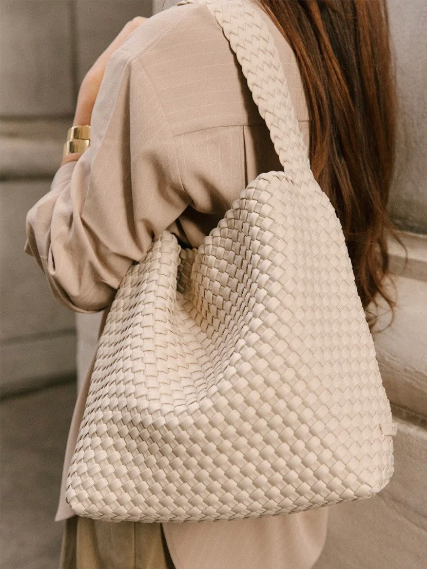 A woman in a beige blazer carries a large woven Naghedi Nomad Hobo in Solid Ecru over her shoulder.