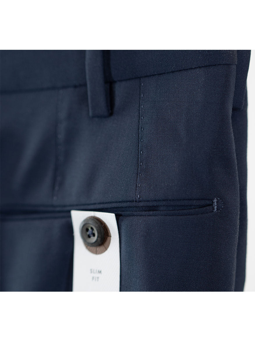 Close-up of the pocket of a PT01 Travel Wool Performance Trousers in Cadet Blue, featuring a brown button attached to a white tag.