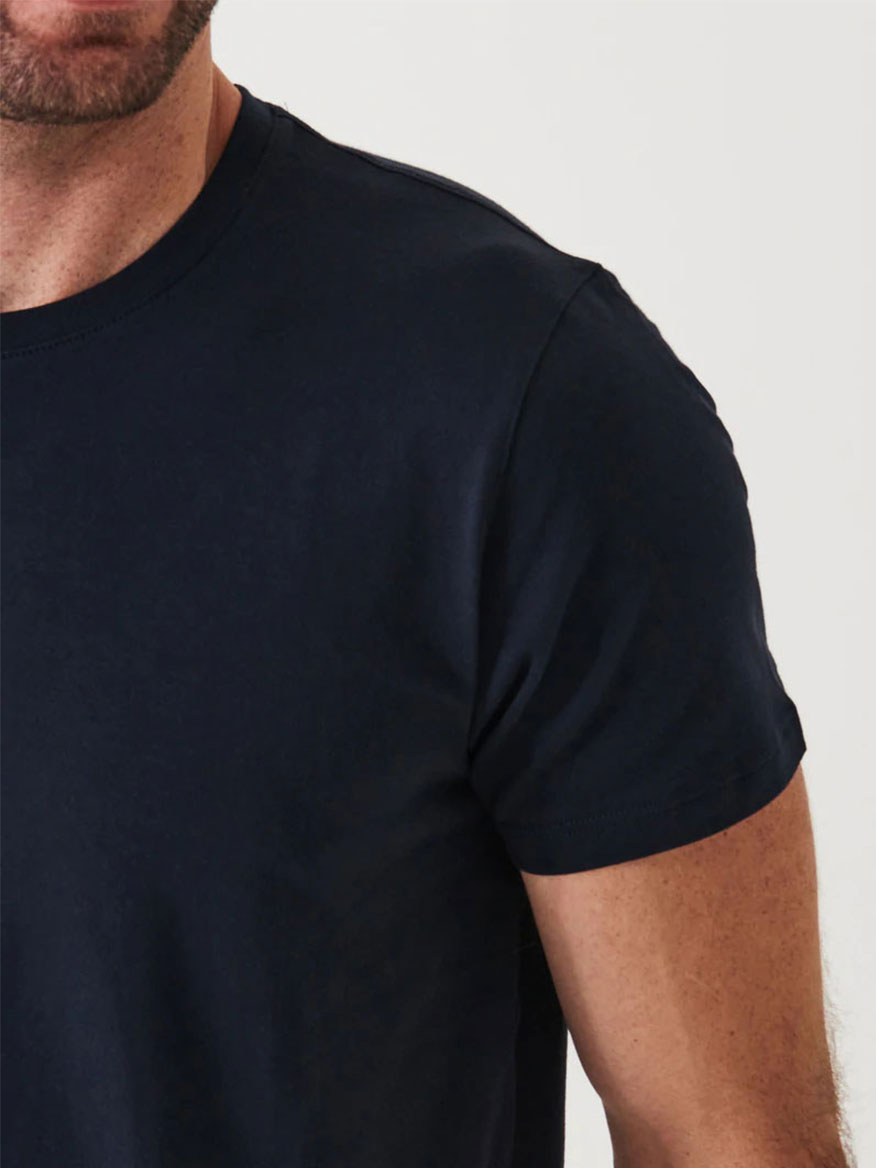 Close-up of a person wearing a navy blue, short-sleeve Patrick Assaraf Iconic T-Shirt in Midnight, made from luxurious Peruvian Pima Cotton, showing the right side of their upper body and arm against a plain background.