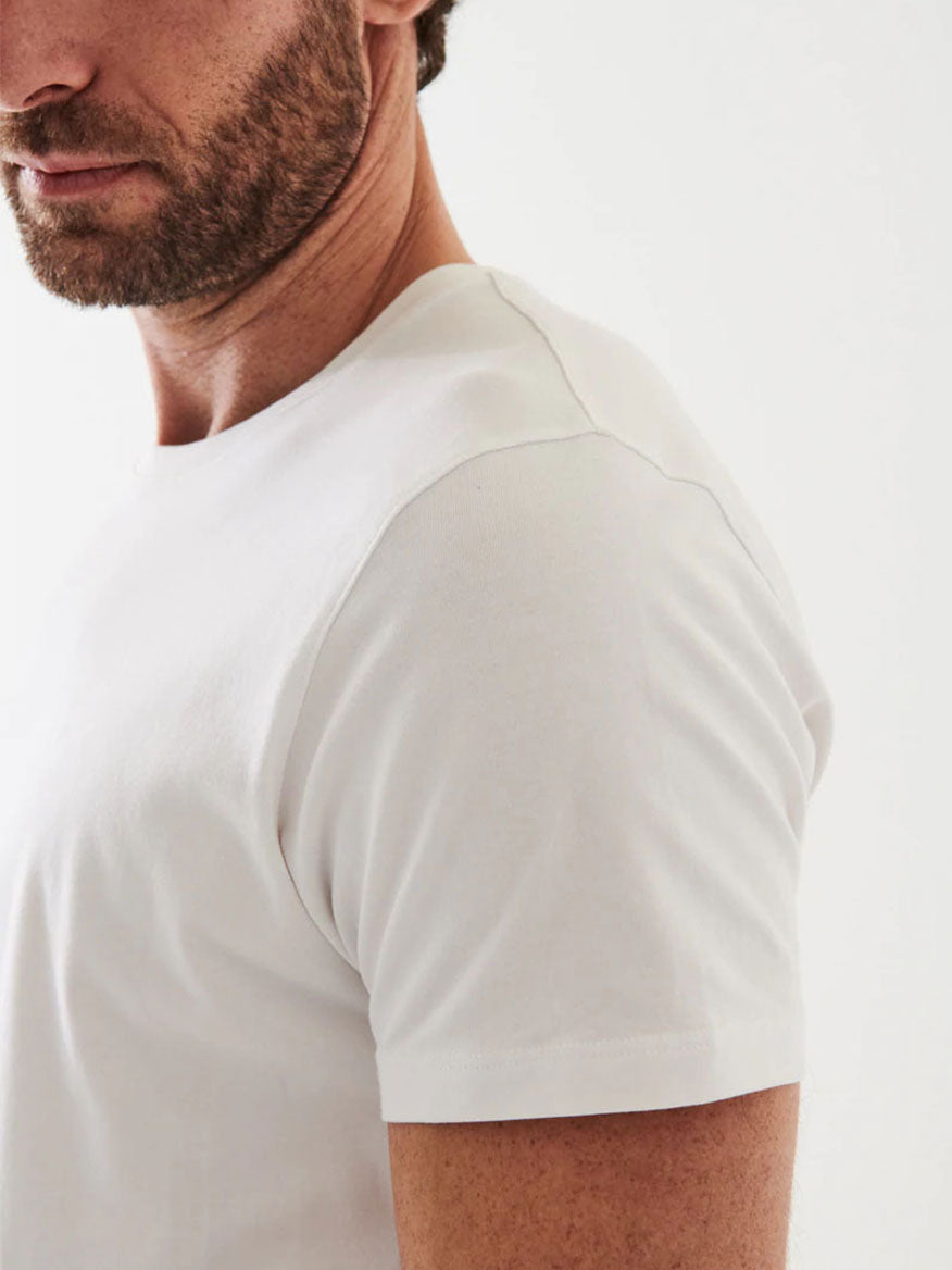 A close-up of a bearded man wearing the Patrick Assaraf Iconic T-Shirt in White, shown from the shoulder to mid-chest, with a neutral background. This versatile layering piece is made from luxurious Peruvian Pima Cotton, offering both comfort and style.