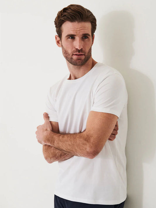 Man with short brown hair and beard wearing a Patrick Assaraf Iconic T-Shirt in White, standing against a white wall with arms slightly crossed.