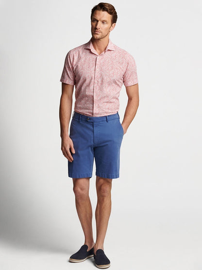 Man posing in a pink printed shirt and Peter Millar Concorde Garment-Dyed Shorts in Riviera Blue.