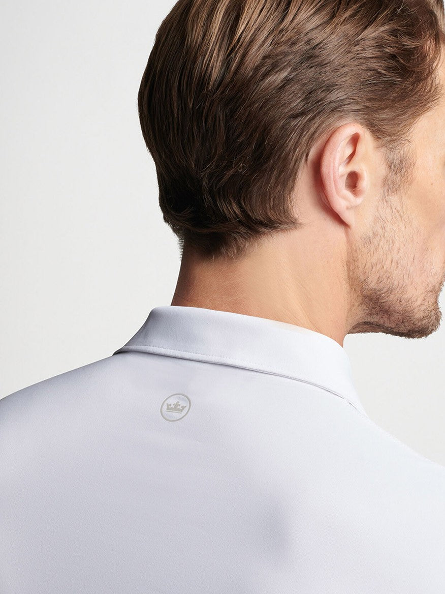 Close-up of a man wearing a Peter Millar Solid Performance Jersey Polo in White with a detailed view of the Peter Millar collar button.