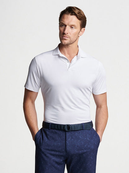Sentence with Product Name: A man posing in a lightweight, white Peter Millar Solid Performance Jersey Polo shirt and patterned blue trousers.