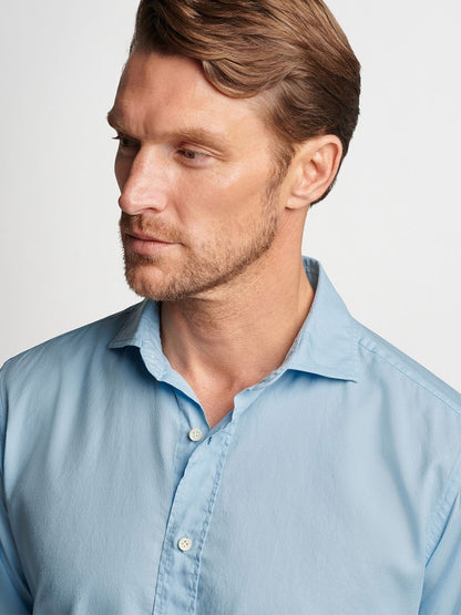 Man in a tailored fit Peter Millar Sojourn Garment-Dyed Cotton Sport Shirt in Blue Frost looking to the side.