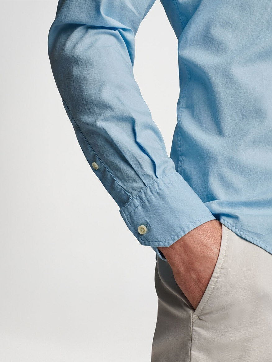 A person standing with elbow bent, wearing a Peter Millar Sojourn Garment-Dyed Cotton Sport Shirt in Blue Frost and beige pants.
