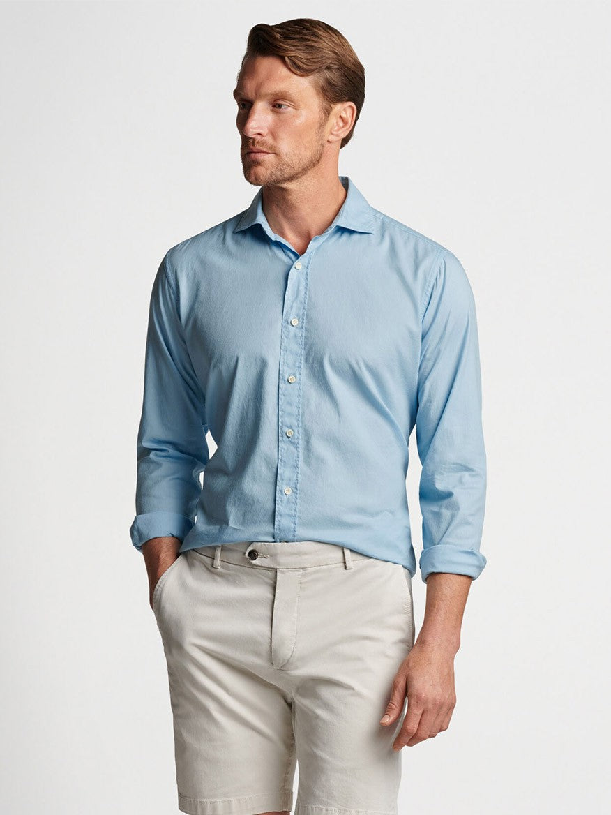 A man wearing a light blue Peter Millar Sojourn Garment-Dyed Cotton Sport Shirt in Blue Frost and beige pants.