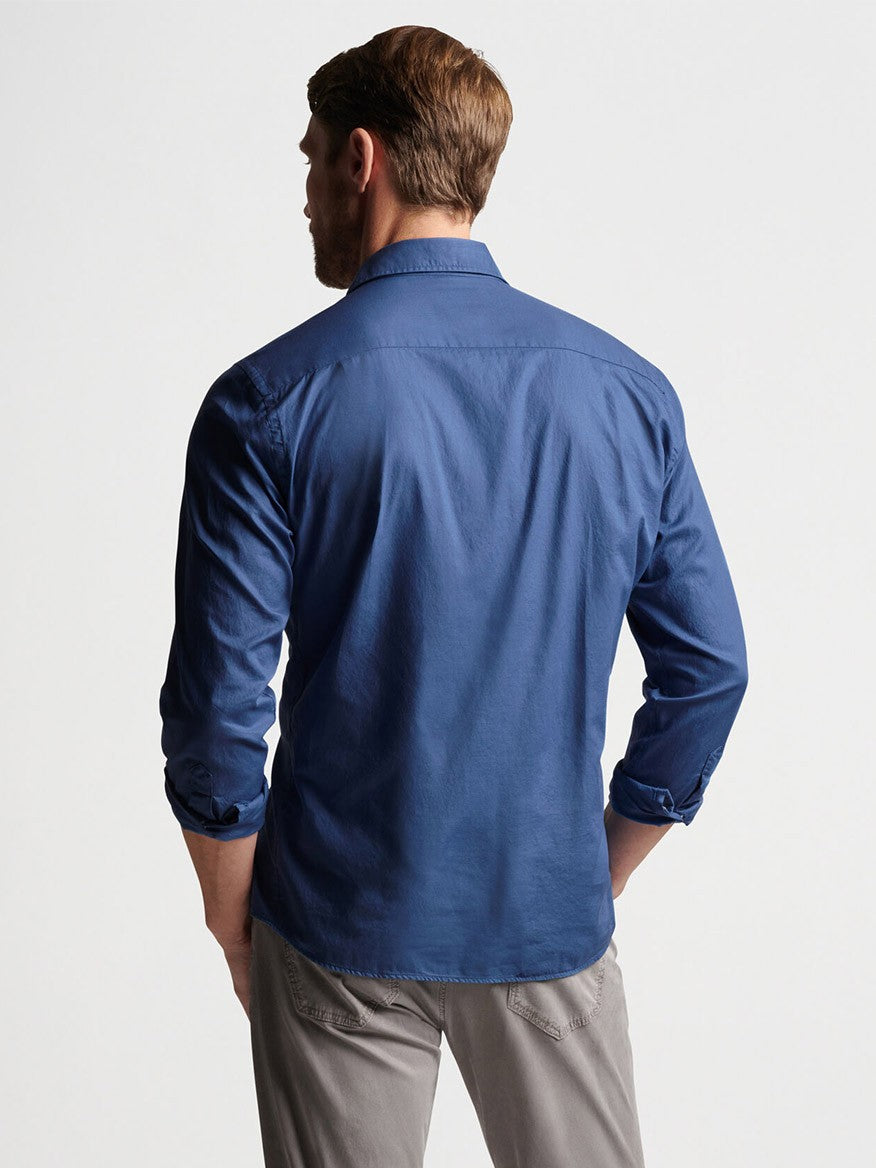 Man standing with his back to the camera, wearing a Peter Millar Sojourn Garment-Dyed Cotton Sport Shirt in Blue Pearl and grey trousers against a neutral background.