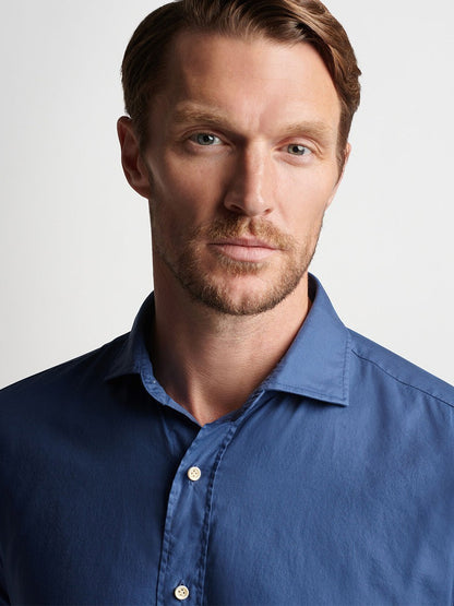 A man with light brown hair wearing a Peter Millar Sojourn Garment-Dyed Cotton Sport Shirt in Blue Pearl, looking directly at the camera with a serious expression.