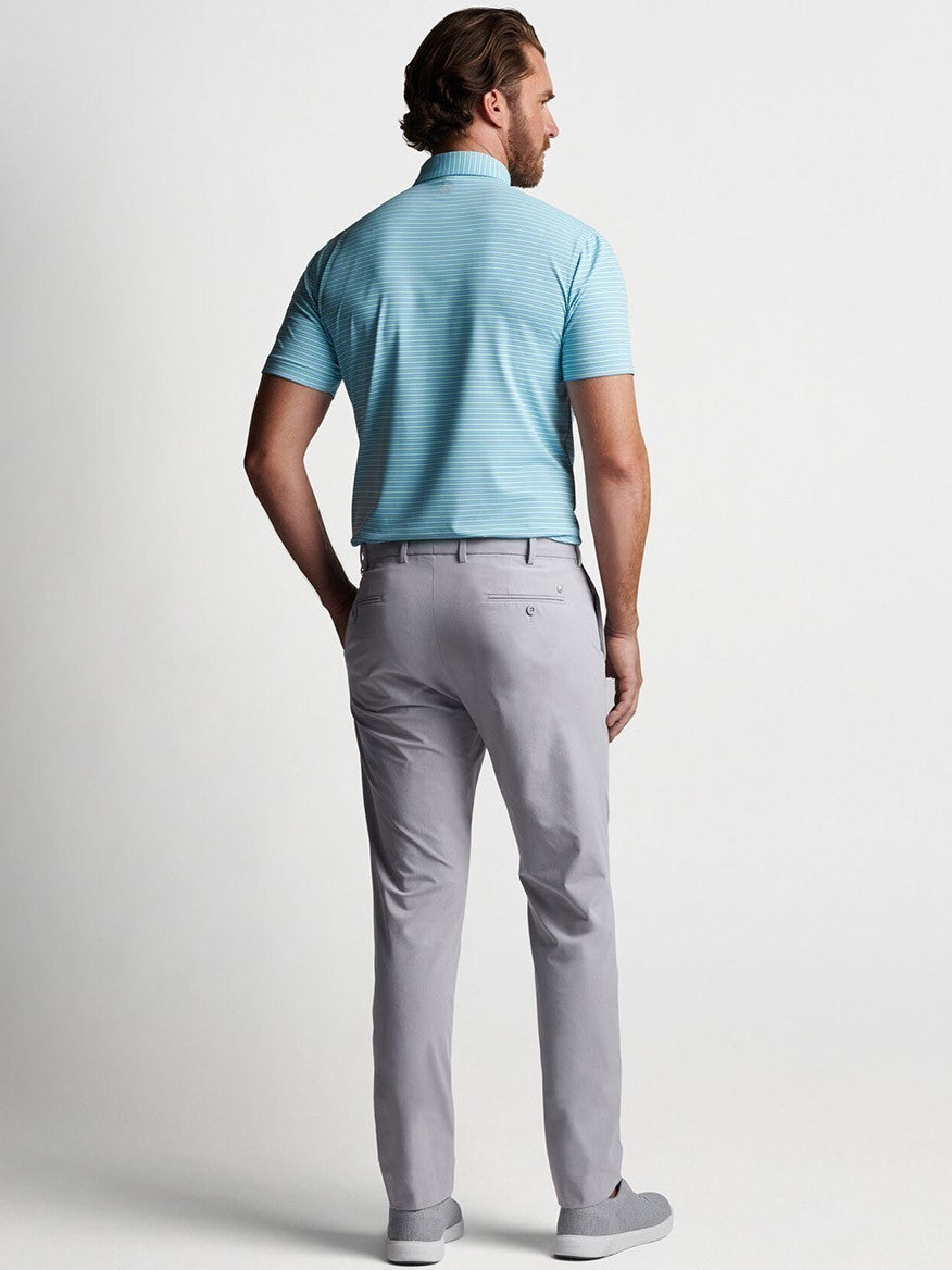 The back view of a man wearing a light blue polo, showcasing his Peter Millar Surge Performance Trouser in Gale Grey.