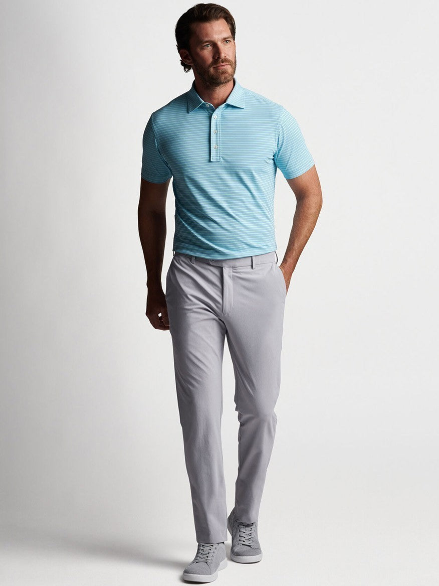 A man wearing a light blue polo shirt and gray Peter Millar Surge Performance Trouser in Gale Grey.