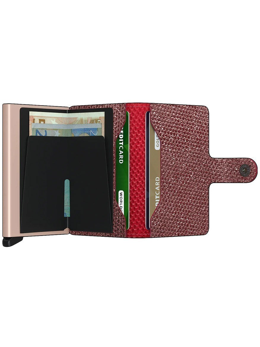 Sentence with replacement: An open, Secrid Miniwallet Sparkle in Red with a rose gold clasp, featuring RFID protection and containing various cards and cash.