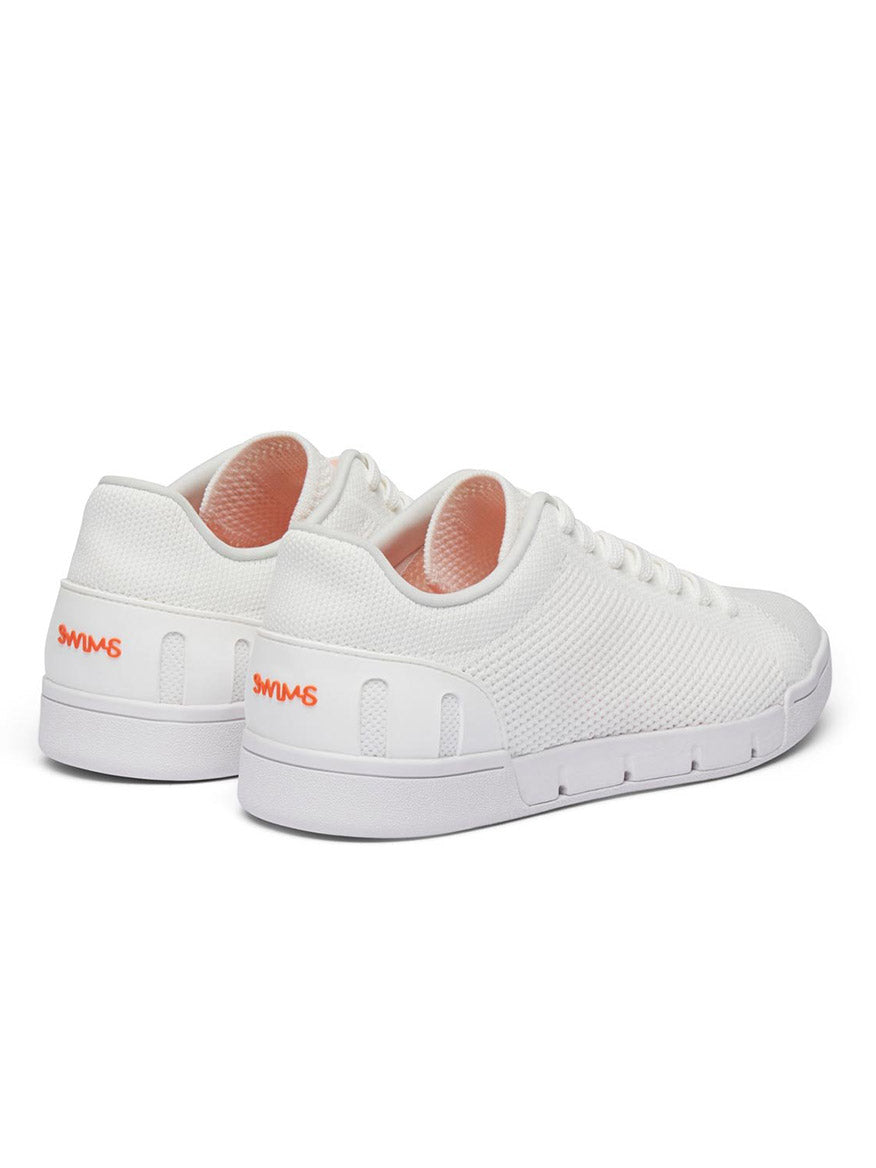 A pair of Swims Breeze Tennis Knit in White with a knitted texture, orange "SWIMS" logo on the heel, and lightweight, breathable white rubber soles.