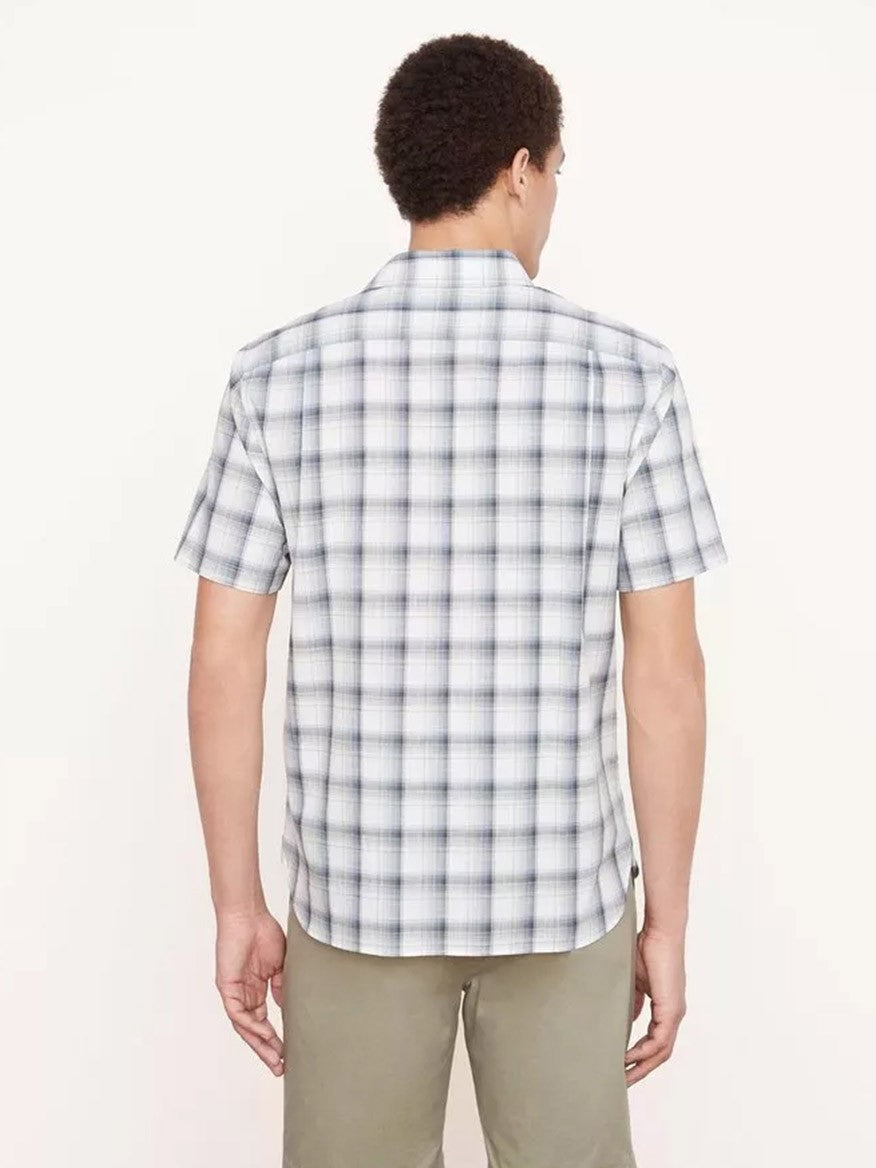 A person with short curly hair is standing with their back to the camera, wearing a Vince Atwater Plaid Short Sleeve Shirt in Celery and olive green pants against a plain background.