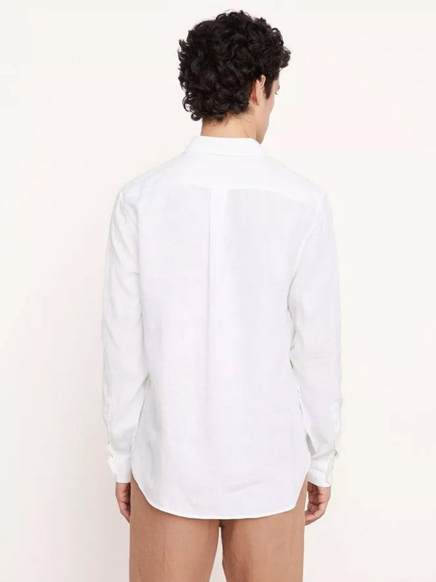 A person with curly hair is standing with their back to the camera, wearing a Vince Linen Long Sleeve in Optic White—a warm-weather staple—and light brown trousers.