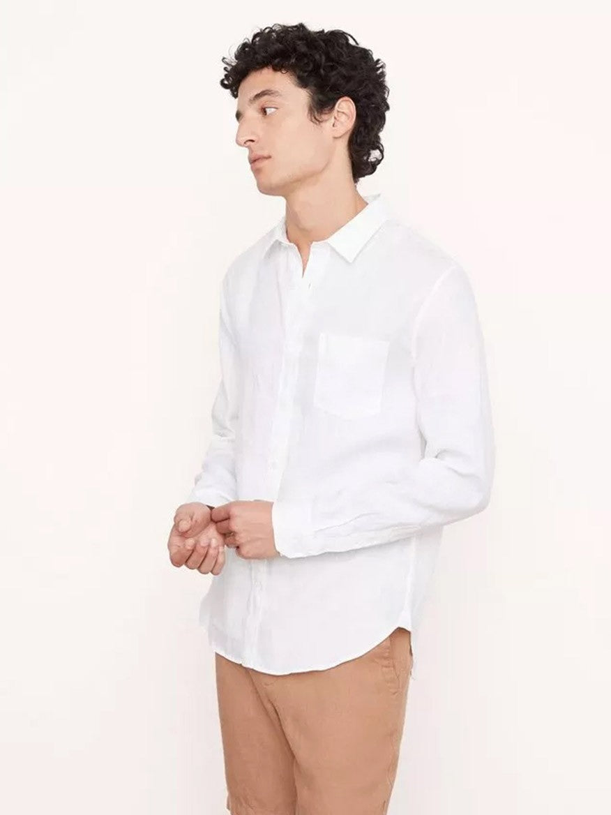 A person with short curly hair is wearing the Vince Linen Long Sleeve in Optic White and light brown pants. They are standing against a plain, light-colored background and looking off to the side.