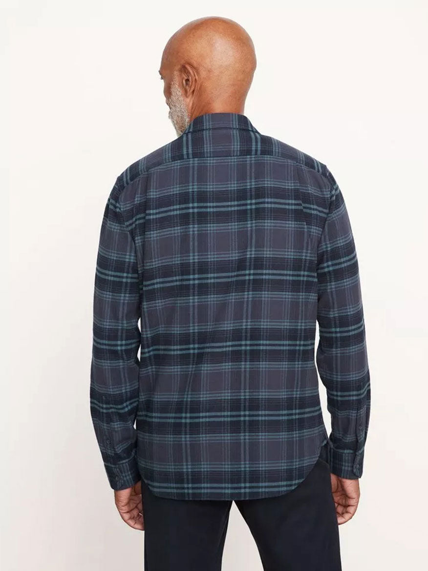 A person with short, white hair and a beard, seen from behind, is wearing a seasonless essential: the Vince Westlight Plaid Long Sleeve Shirt in Nightfall, an ultra-soft cotton button-down in a subtle plaid of blue and black, paired with black pants.
