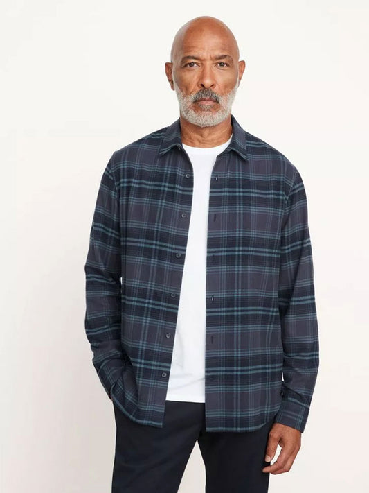A man with a mustache and beard, dressed in a Vince Westlight Plaid Long Sleeve Shirt in Nightfall over a white t-shirt, stands against a plain background.