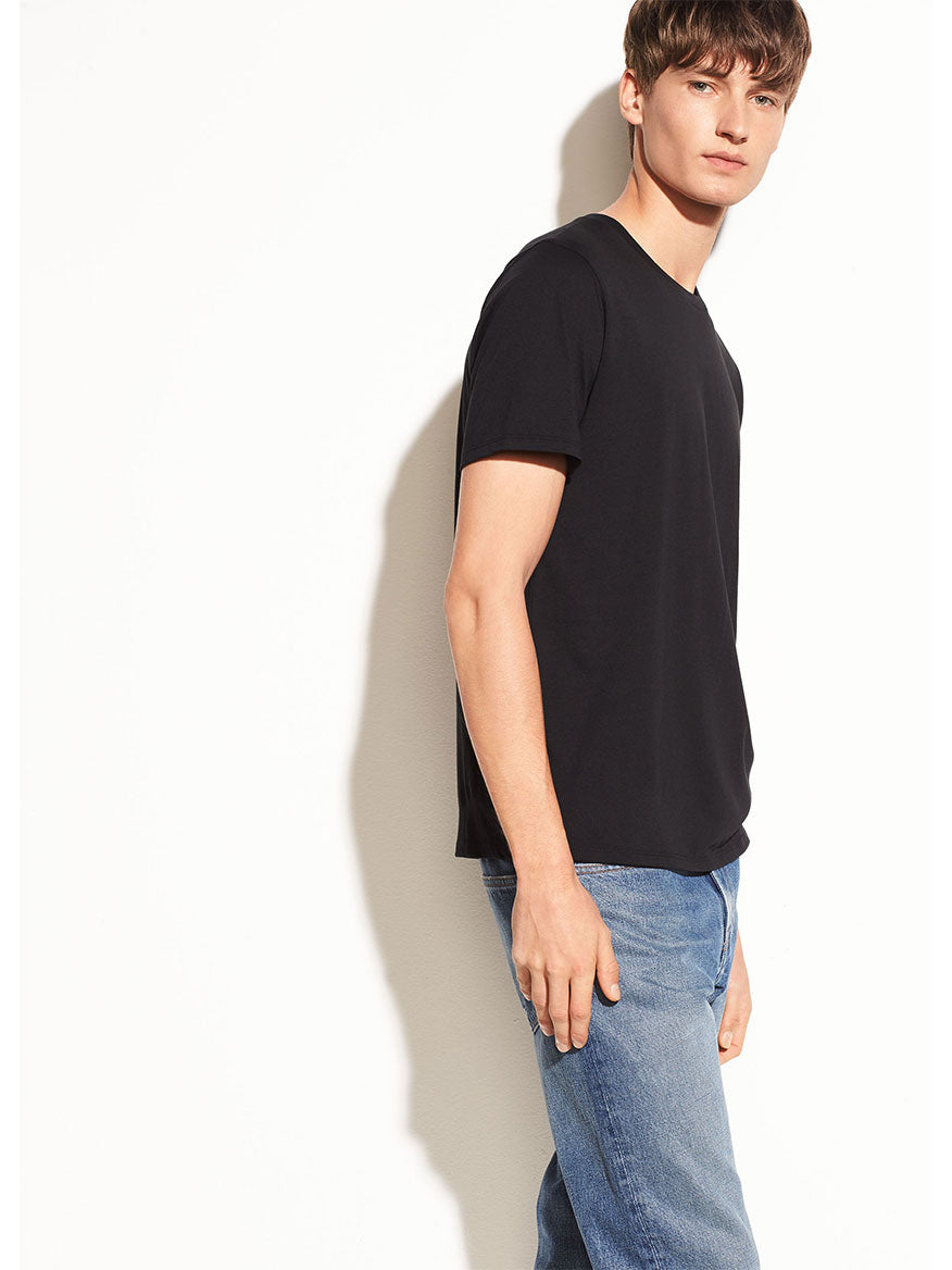 Young man in a Vince Crew Neck T-Shirt in Black and blue jeans standing against a white background.