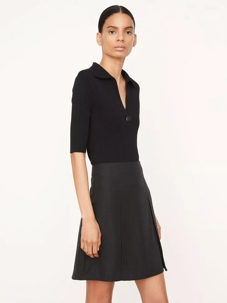 A person is wearing a Vince Pleated Short Skirt in black, featuring a cotton-blend design with a collar and short sleeves, while standing against a light background.