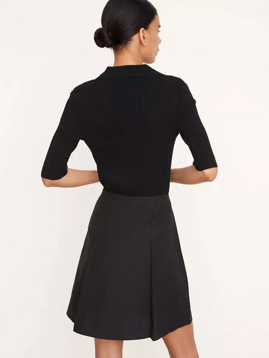A person wearing a Vince Pleated Short Skirt in black and a matching top faces away, their hair elegantly styled in a bun.