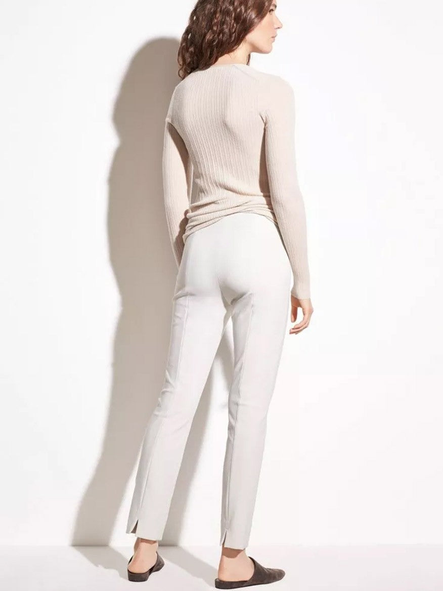 A woman stands facing away from the camera, wearing a beige sweater and Vince Stitch Front Seam Ponte Legging in Gesso with an elasticated waistband, with a shadow cast on a white background.