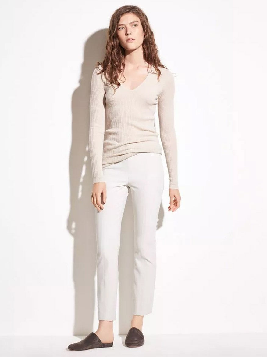 A person wearing Vince Stitch Front Seam Ponte Legging in Gesso, a white long-sleeve top, and dark slip-on shoes stands against a neutral background.