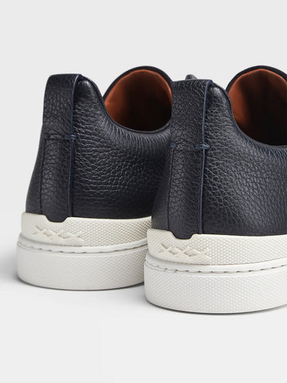 A close-up of the back of a pair of navy blue grained leather and suede Zegna sneakers with white soles.