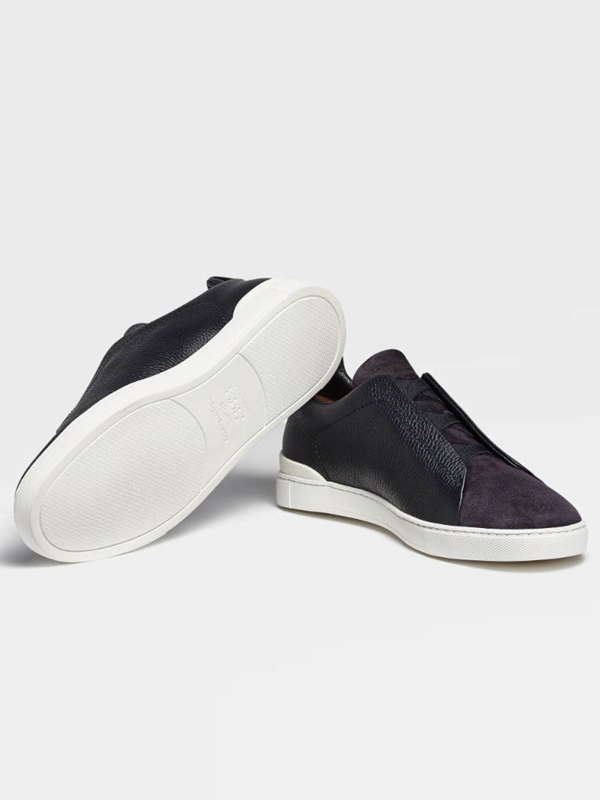 A pair of navy blue Zegna slip-on sneakers with white soles displayed against a grey background.