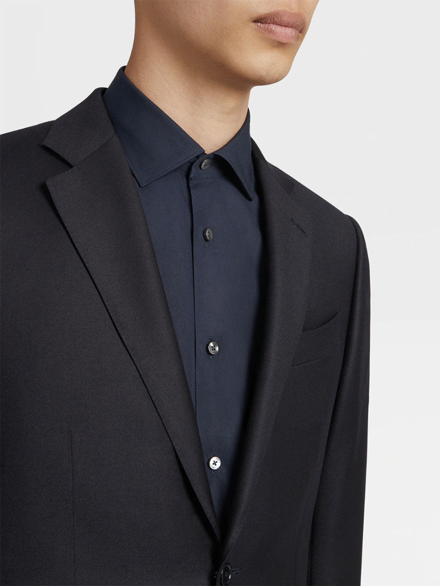 A person dressed in a dark blazer over a navy blue Zegna Navy Blue Milano Trofeo™ Wool Suit. The image captures the upper torso and part of the face, with a focus on the clothing details.