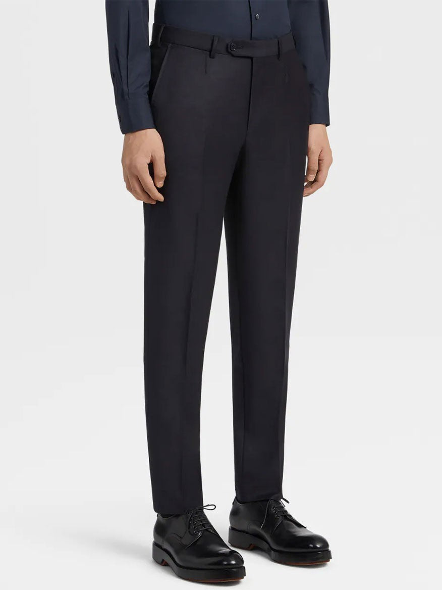 A person wearing dark dress pants, a dark shirt, and black dress shoes stands with arms relaxed at their sides against a plain background. They exude sophistication in their Zegna Navy Blue Milano Trofeo™ Wool Suit.