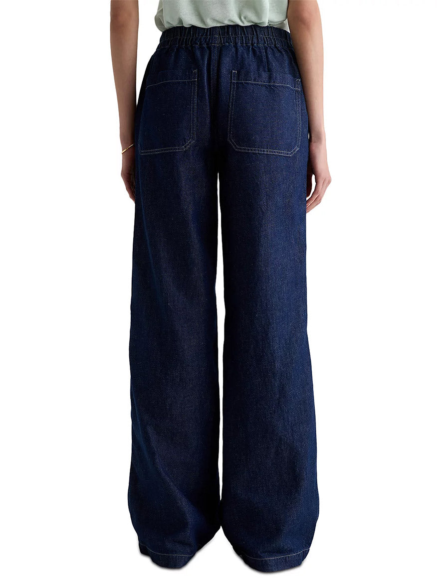 A person is seen from behind wearing AG Jeans Adria Cinched Jean Low-Rise Wide Leg in Napa, featuring dark blue denim, an elastic waistband, and two large back pockets.