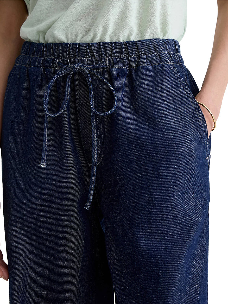 Close-up of a person wearing AG Jeans Adria Cinched Jean Low-Rise Wide Leg in Napa with a drawstring, styled with a light top and one hand casually slipped into the pocket.