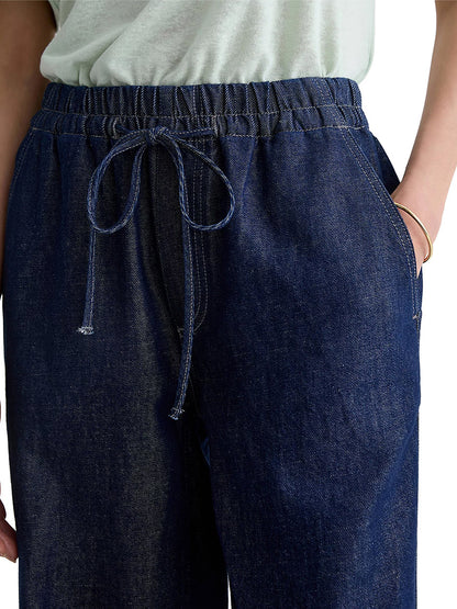 Close-up of a person wearing AG Jeans Adria Cinched Jean Low-Rise Wide Leg in Napa with a drawstring, styled with a light top and one hand casually slipped into the pocket.