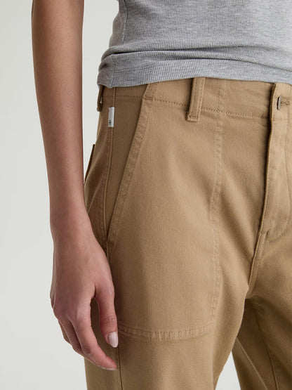 A person shown from the waist to mid-thigh wears a gray sleeveless top paired with AG Jeans Analeigh Mid-Rise Utility Pant in Khaki Sand, featuring front pockets.