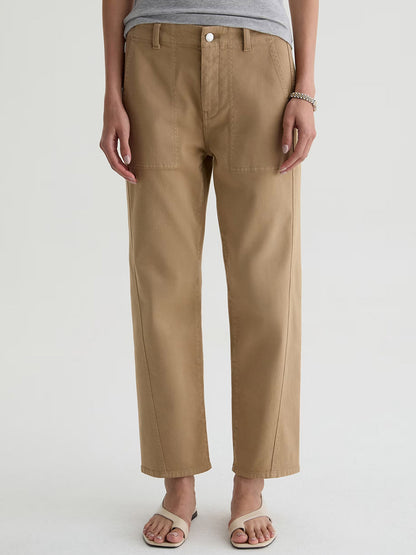 Person wearing AG Jeans Analeigh Mid-Rise Utility Pant in Khaki Sand, a grey top, sandals, and a bracelet, standing against a plain light background.
