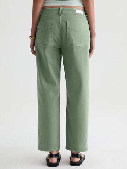 Person wearing AG Jeans Analeigh Mid-Rise Utility Pant in Sulfur Faded Moss, black sandals, and a gold bracelet, shown from the back against a plain background.