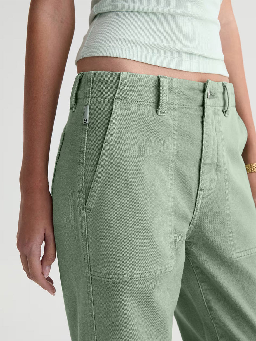 Model shown from mid-torso to mid-thigh wearing the AG Jeans Analeigh Mid-Rise Utility Pant in Sulfur Faded Moss, styled with a matching light green ribbed tank top.