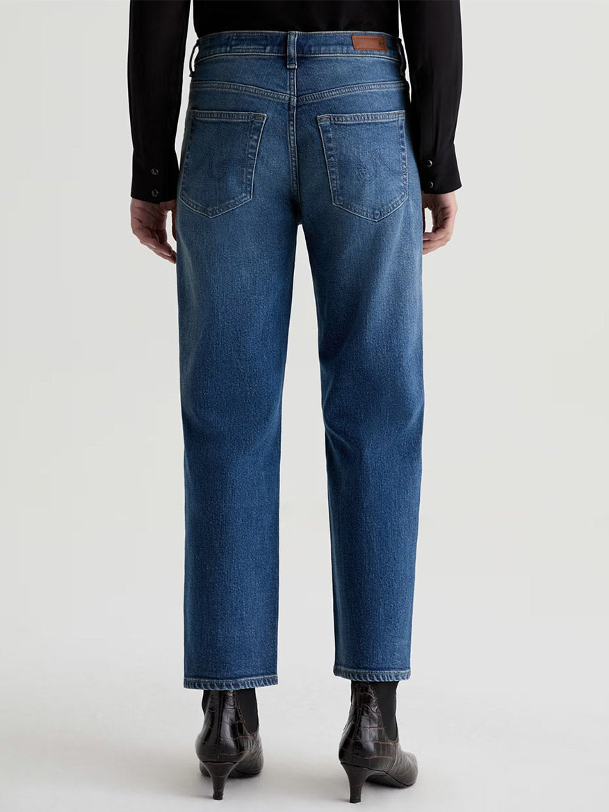 Someone is shown from the back wearing AG Jeans Brinley Mid-Rise Straight in Hotel California, styled with a black shirt and black heeled boots.