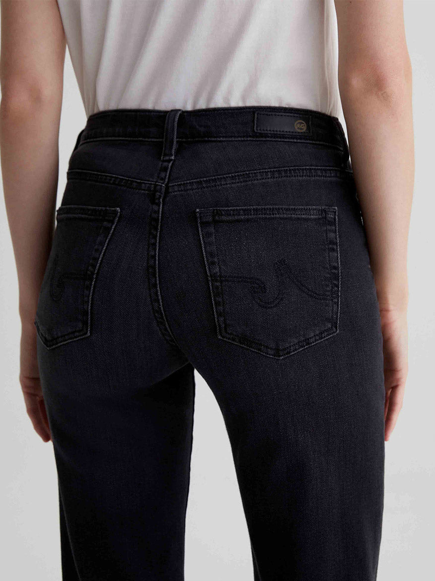 Rear view of a person in the AG Jeans Brinley Mid-Rise Straight in Glasgow, featuring embroidered back pockets and crafted from comfort stretch denim.